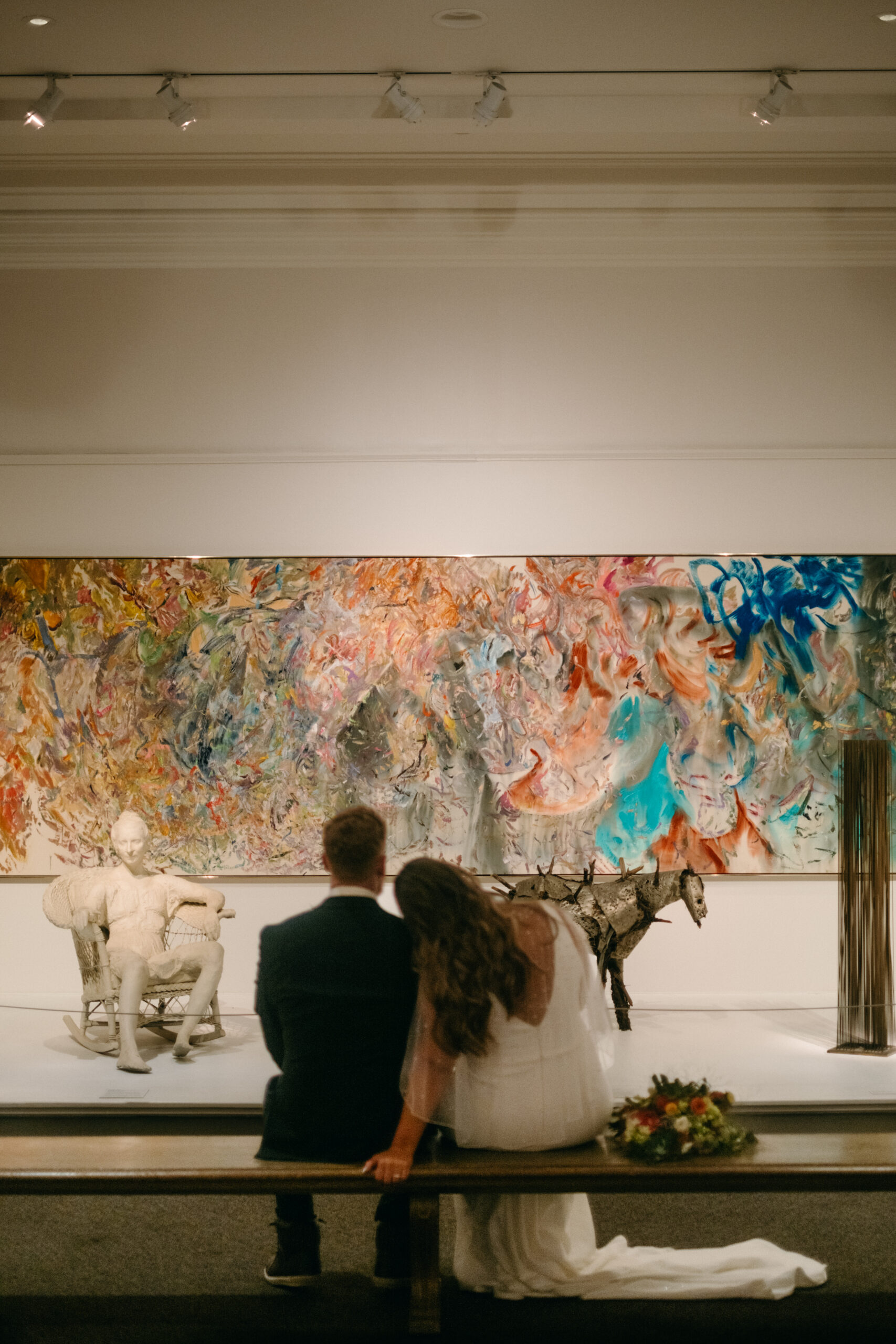 bride leans on grooms shoulder view from behind as they stare at painting in museum