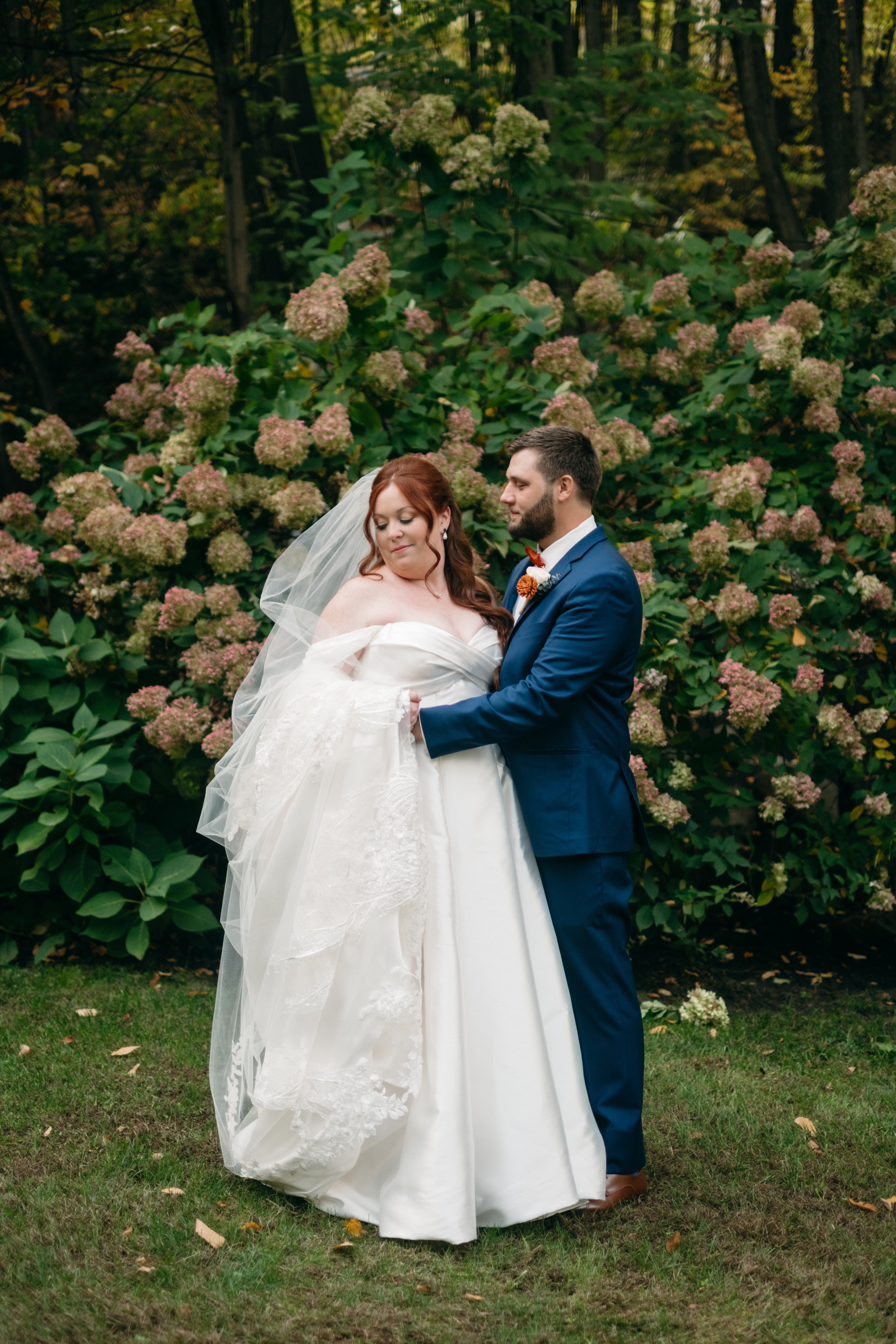 groom looking at bride who holds dress against pink hydrangeas weddingg